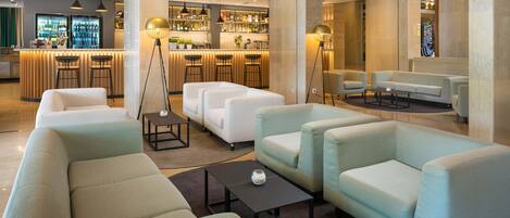 Un moderno vestíbulo de hotel con zona de bar, arreglos de asientos y mostrador de recepción.