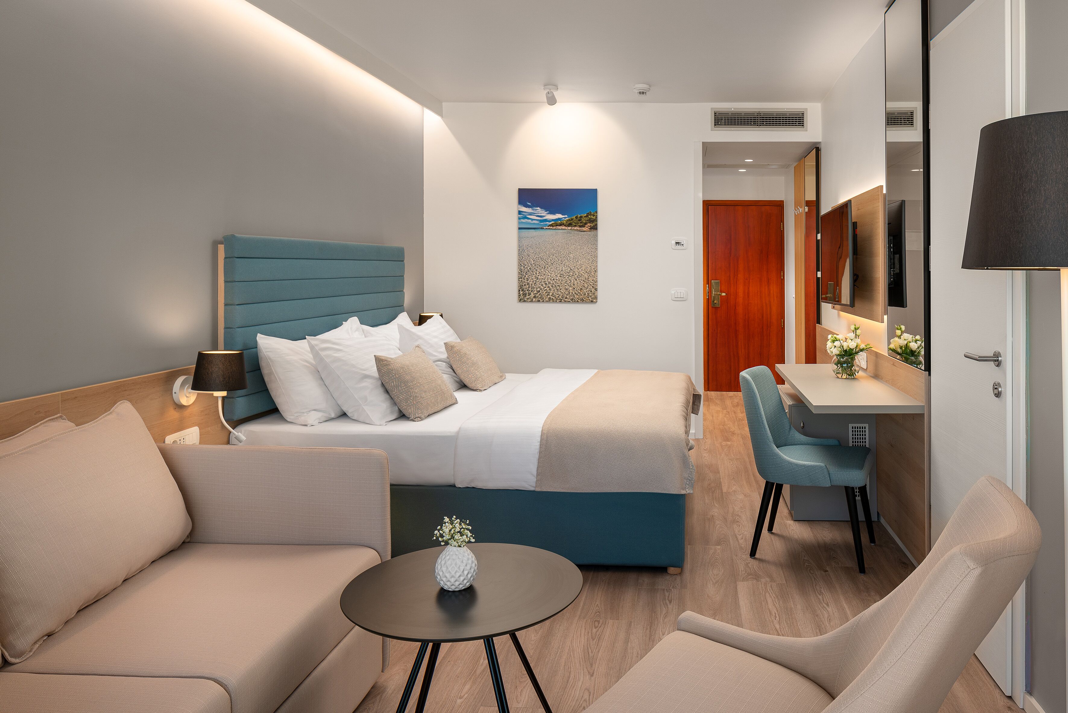 A modern hotel room with a bed, a desk, a chair, and a small table.