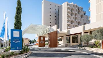 Una entrada de hotel moderna con un vestíbulo cubierto, un letrero llamativo y un árbol alto.
