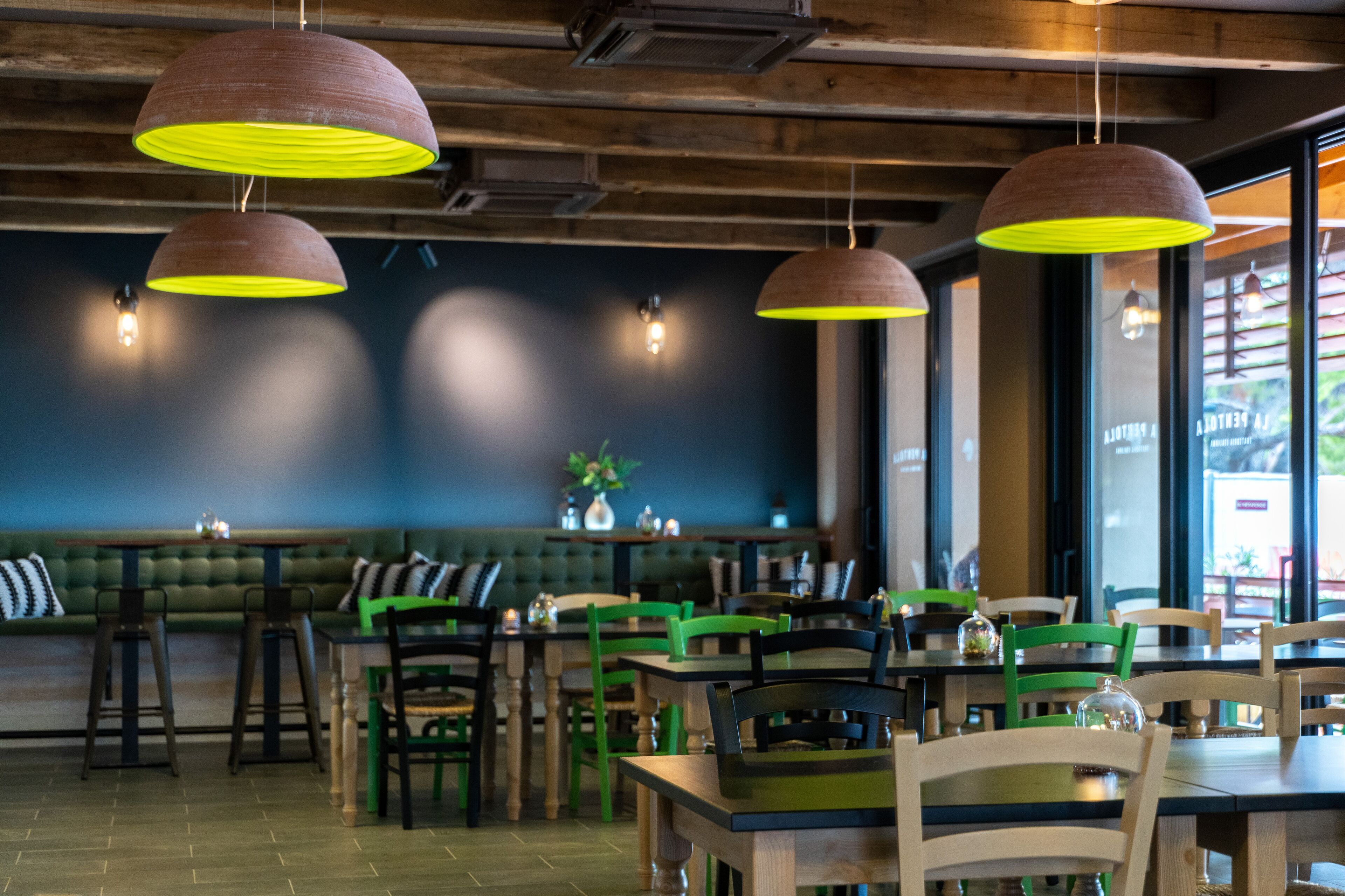A restaurant interior with wooden tables, green chairs, and hanging pendant lights.