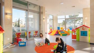 A spacious indoor play area with large windows, a soft orange carpet, and colorful play structures.