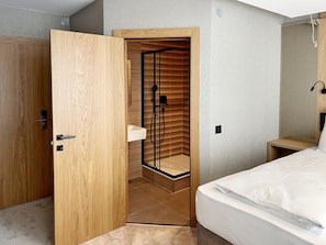 A modern bedroom with a wooden wardrobe, a built-in shower with a glass door, and a bedside table with a lamp. - DORMERO Hotel Reutlingen (Reutlingen)