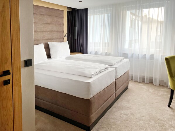 A double bed with a wooden headboard, a bedside table, and a chair. - DORMERO Hotel Reutlingen (Reutlingen)