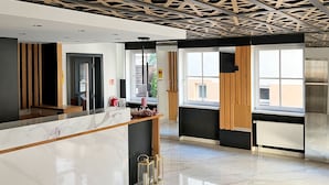 A modern reception area with a marble counter, wooden accents, and a geometric ceiling design. - DORMERO Hotel Reutlingen (Reutlingen)