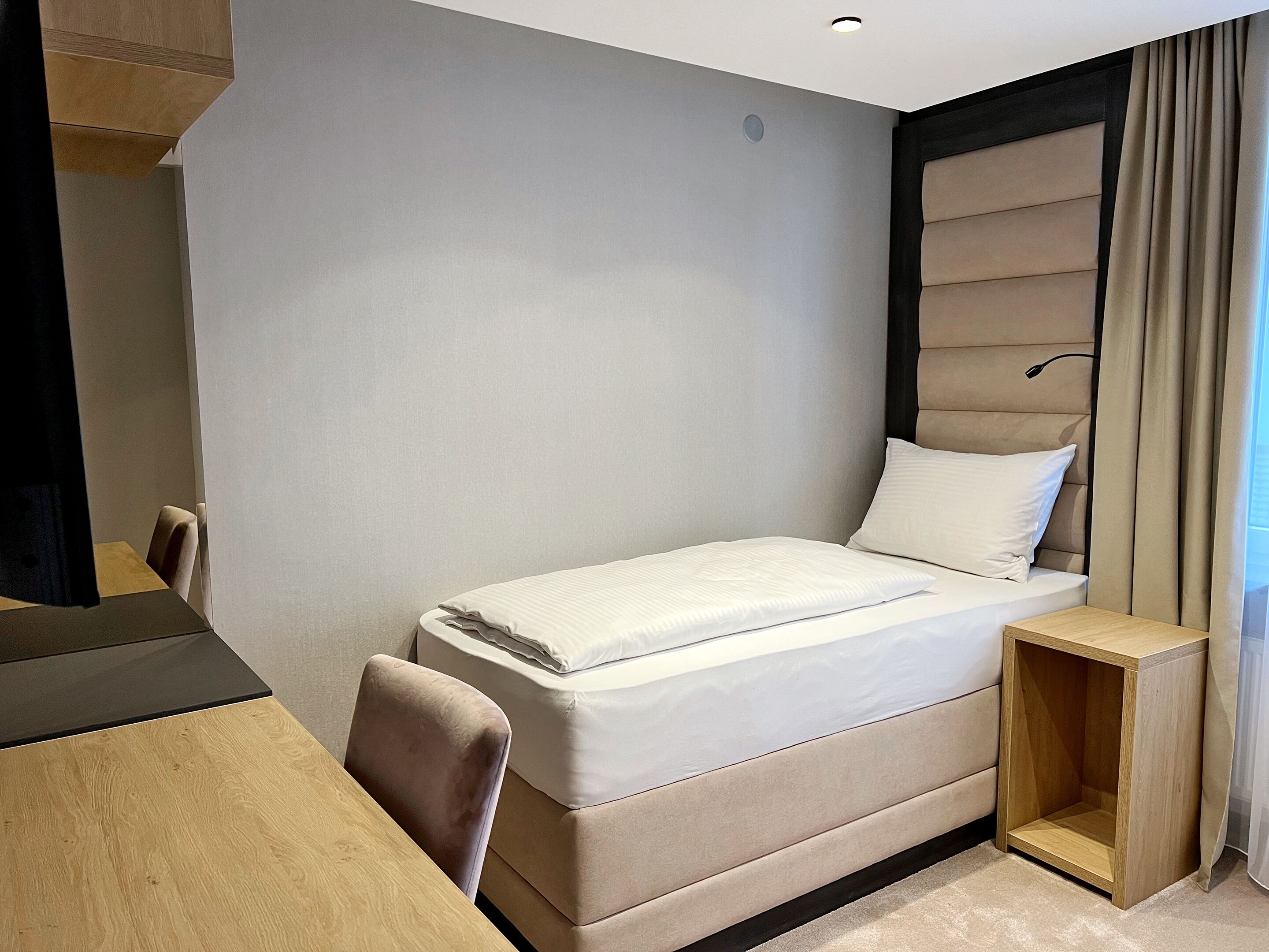 Una habitación de hotel moderna con una cama, una mesita de madera, una silla y un mueble pequeño de madera.