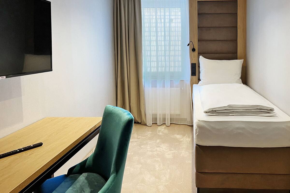 Una habitación de hotel con cama, escritorio, silla, televisor y ventana con cortinas.