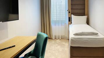 A hotel room with a bed, a desk, a chair, a television, and a window with curtains.
