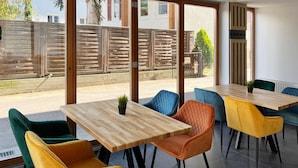 A modern dining area with wooden tables and colorful chairs, large windows, and a view of the outside. - DORMERO Hotel Reutlingen (Reutlingen)
