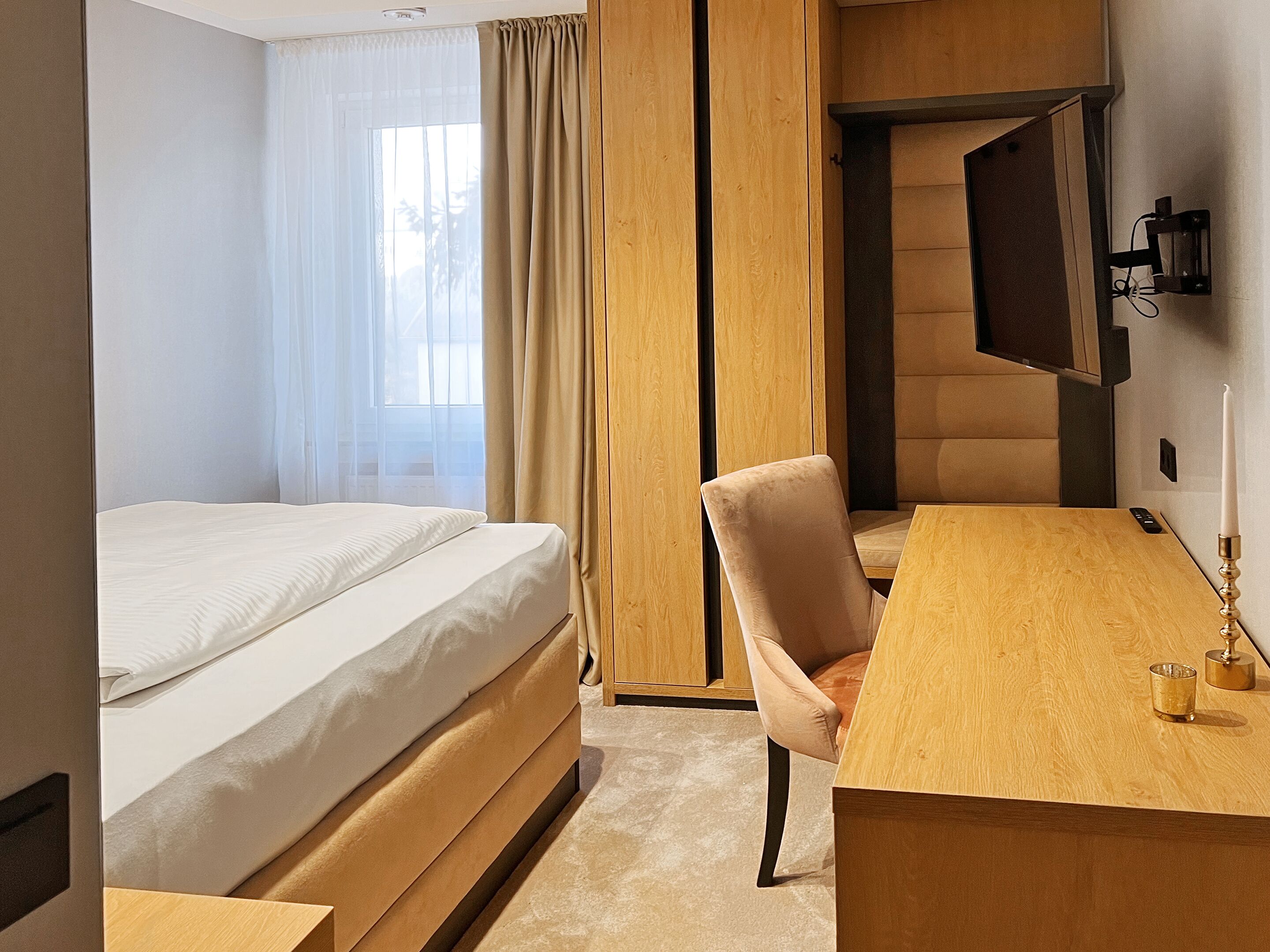 A hotel room with a bed, a desk, a chair, a television, and a window with curtains.