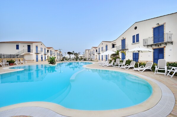 A swimming pool with lounge chairs and a building with balconies. - Scala Dei Turchi Resort (Realmonte)