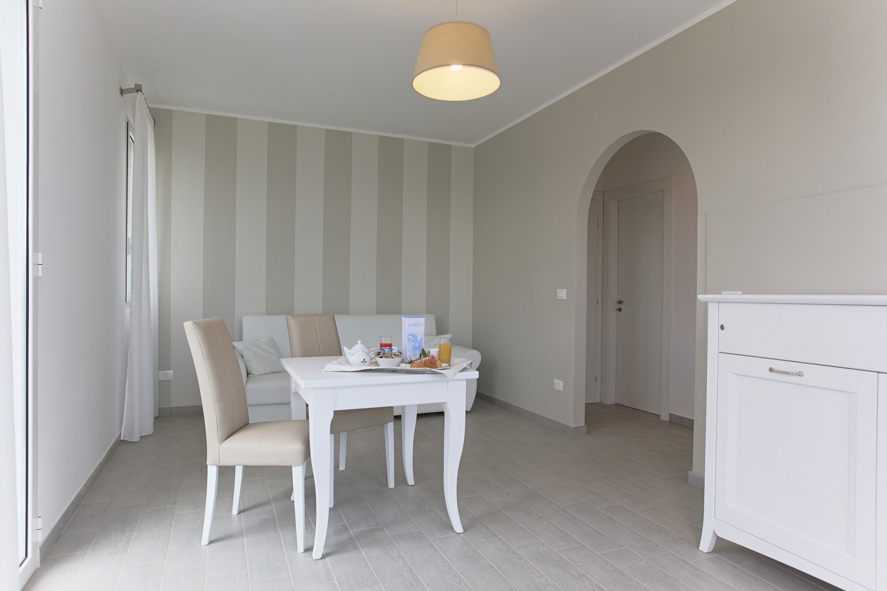 A dining area with a white table and chairs, a striped wall, and a ceiling light.