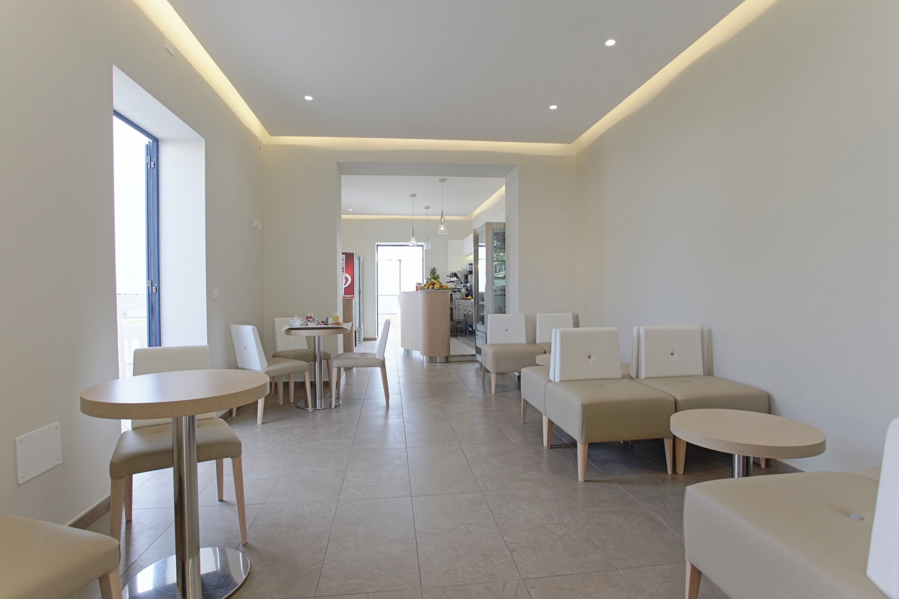Una hall d'albergo moderna e ben illuminata, con zone salotto, una reception e una cucina sullo sfondo.