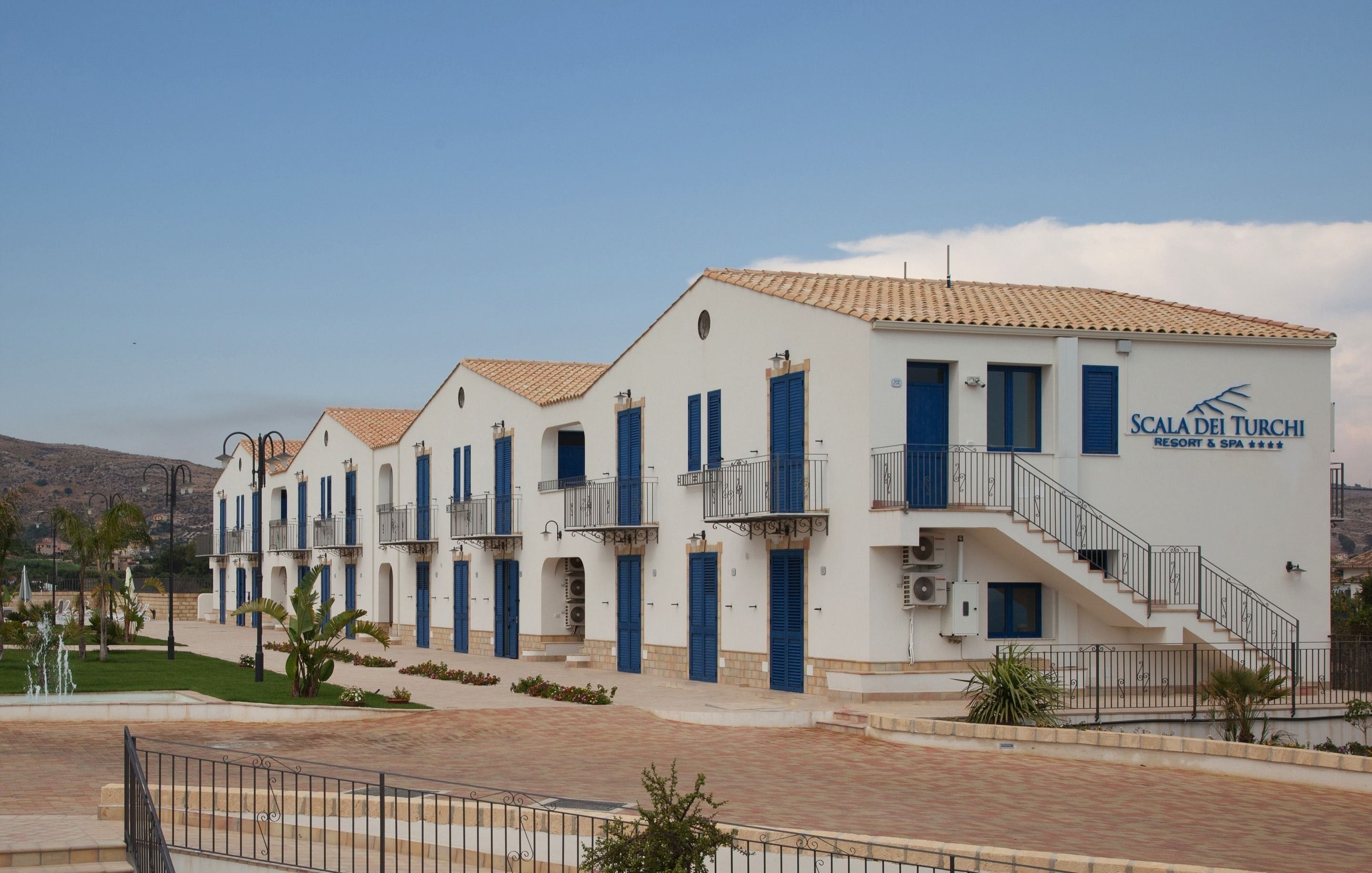 Una hilera de edificios blancos con contraventanas azules y balcones, identificada como 