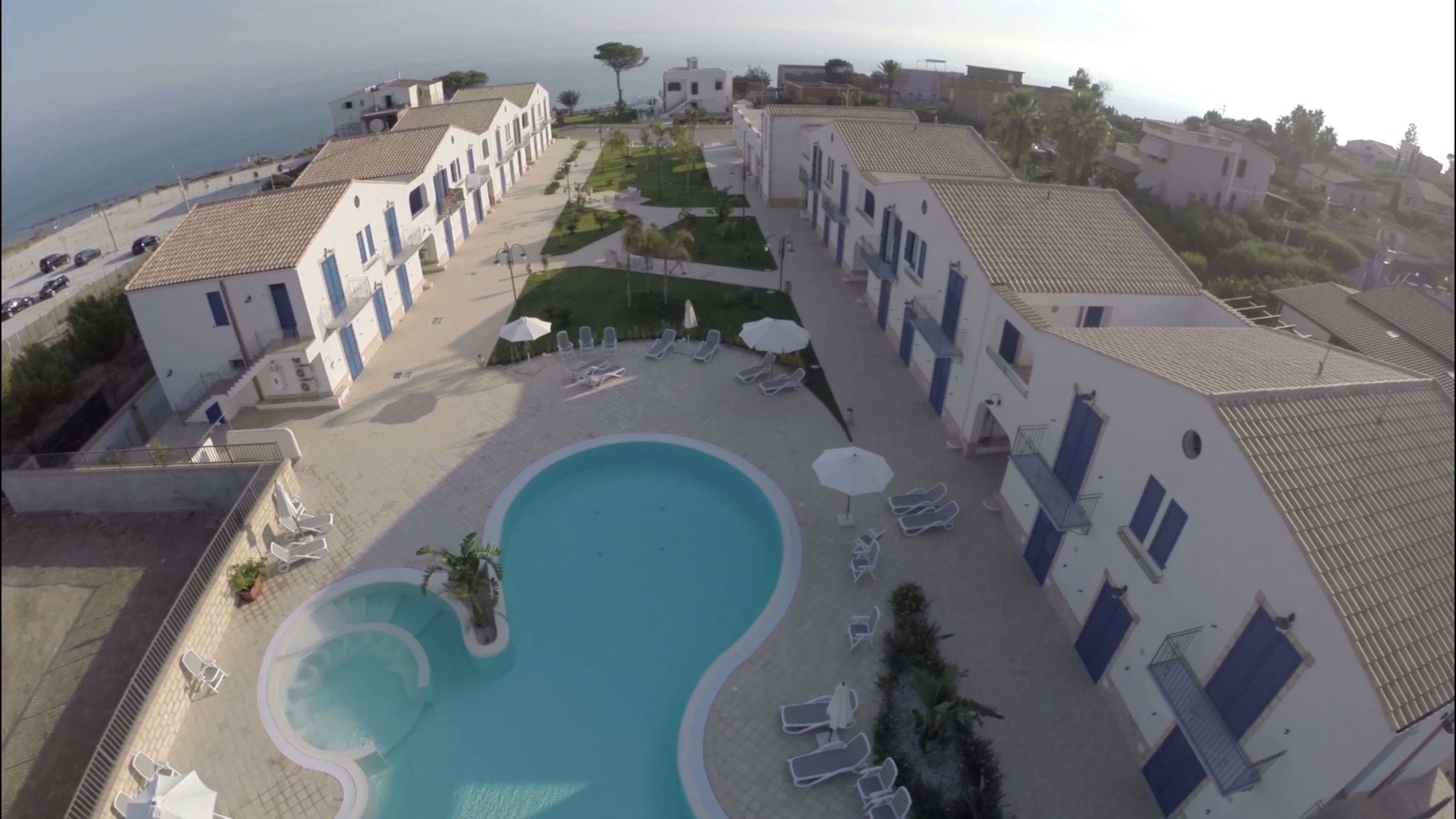 Een hotel met een zwembad, omringd door ligbedden en parasols, met uitzicht op de zee en een mediterrane bouwstijl.