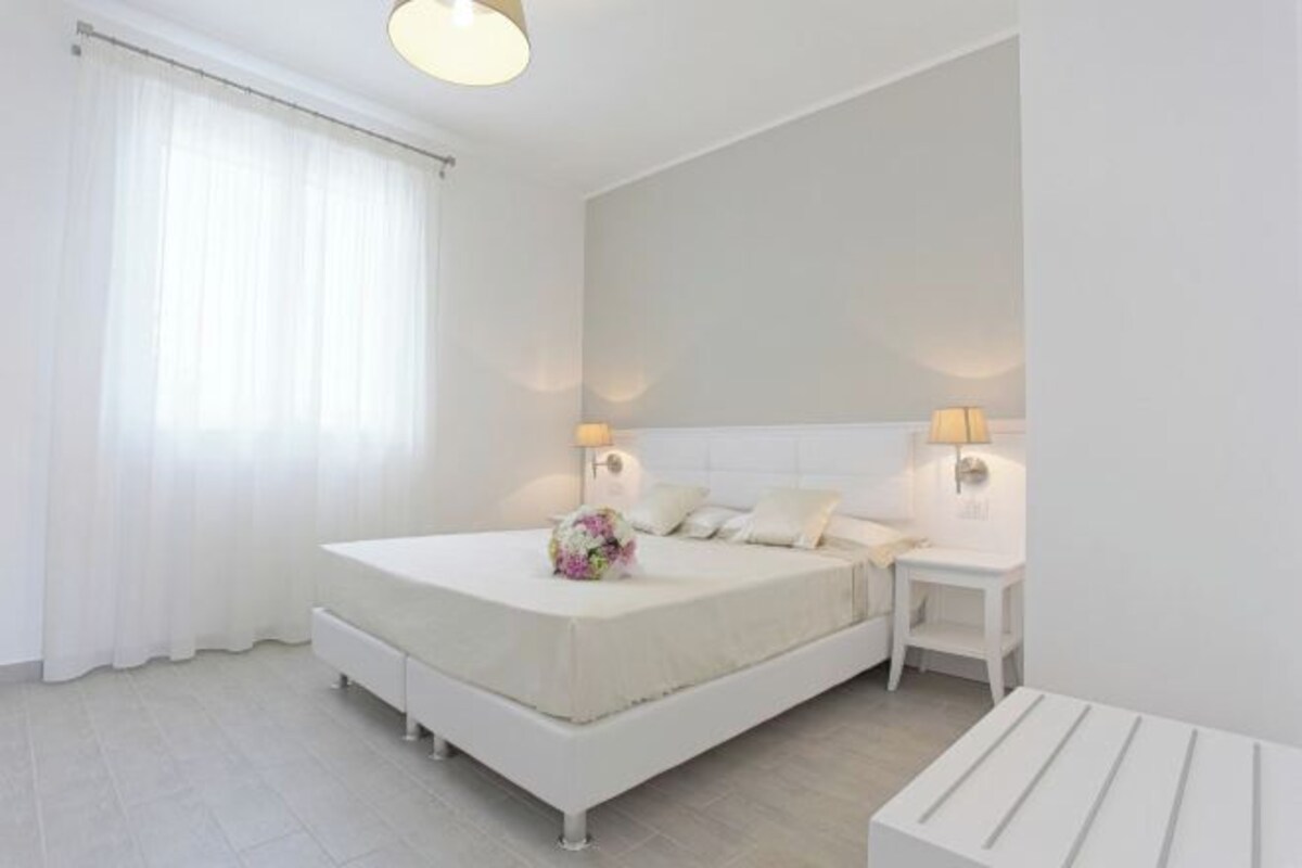 A white bedroom with a bed, bedside lamps, and a small table.