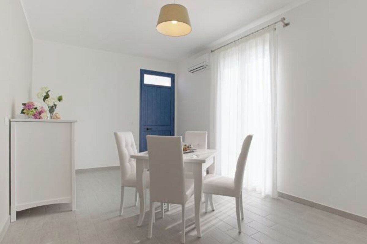 A dining area with a white table, four chairs, a blue door, and a light fixture.
