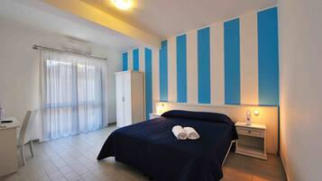 Ein Hotelzimmer mit Bett, Schreibtisch, Stuhl, Kleiderschrank und Nachttisch mit Lampe.