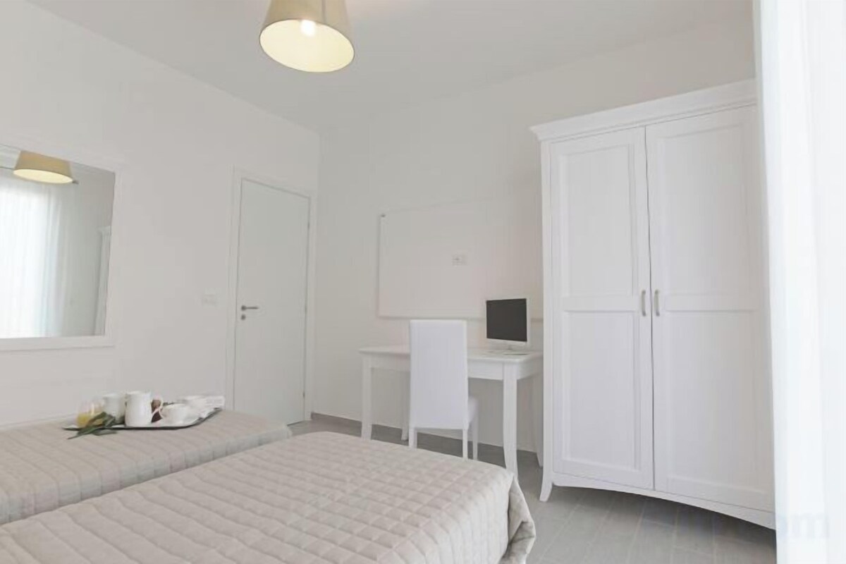 A bedroom with two beds, a desk, a wardrobe, and a mirror.