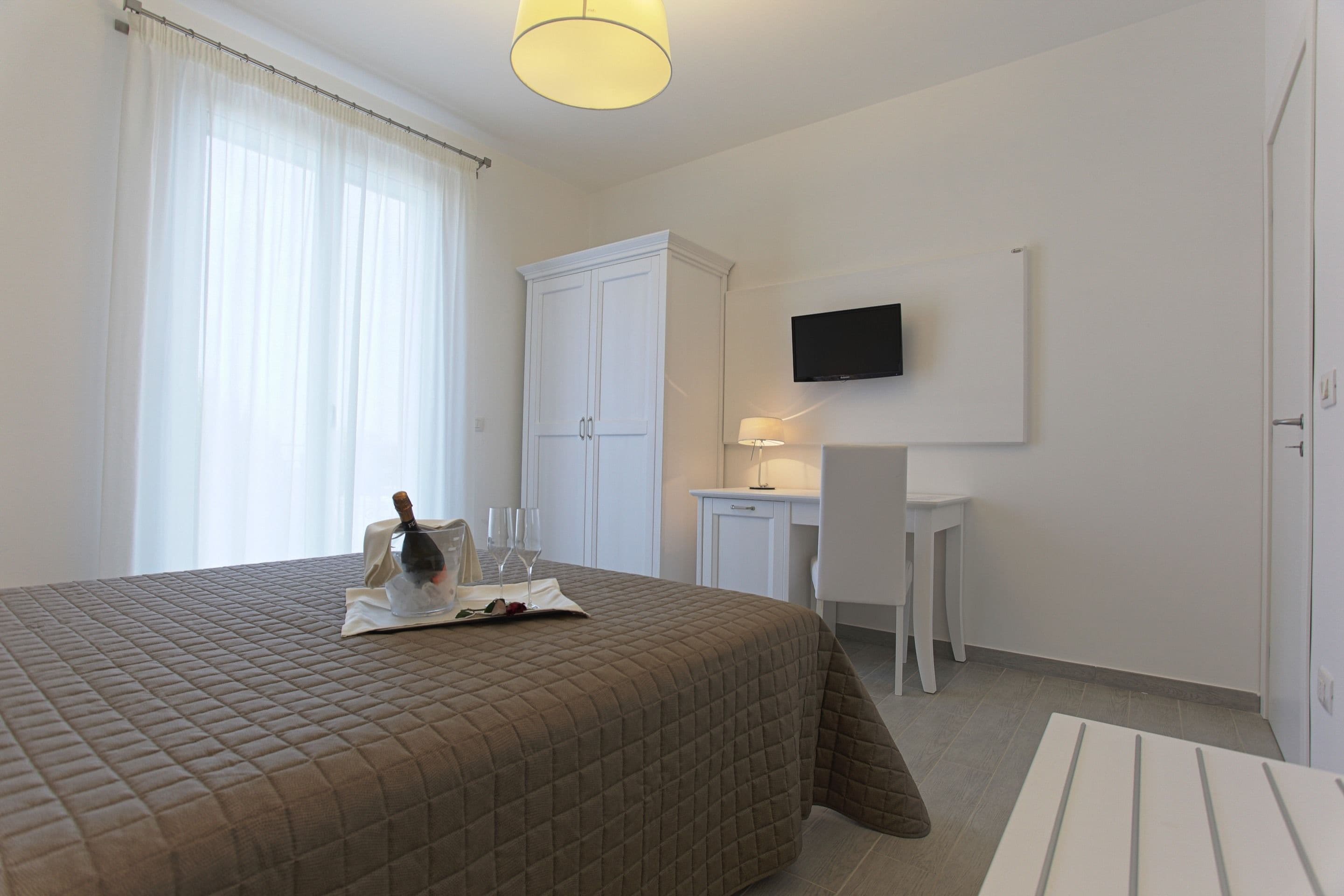 A hotel room with a large bed, a desk, a television, and a wardrobe.