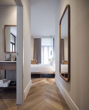 A hotel room with a wooden herringbone floor, a bed with a white duvet, a bedside table with a lamp, and a large mirror on the wall. - Room Mate Oliveira – City Centre, Valencia (Valencia)