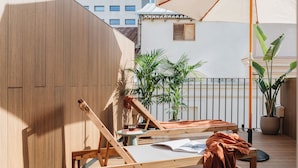 Une terrasse en bois avec un fauteuil de relaxation, une table avec un livre et un grand parasol.