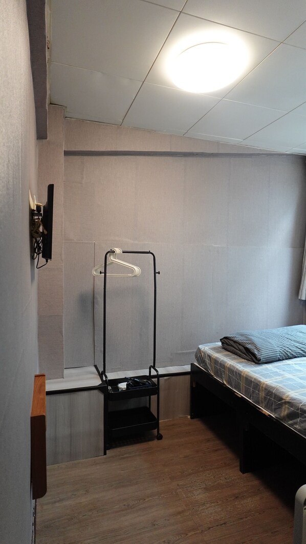 A small, compact room with a bed, a clothing rack, and a shelf unit.