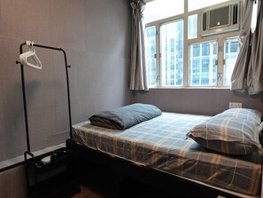 A single bed with a plaid bedspread and pillows, a black floor lamp, and a window with curtains.