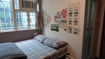 A small, single-bed room with a window, a radiator, and a wall decorated with a cityscape mural.