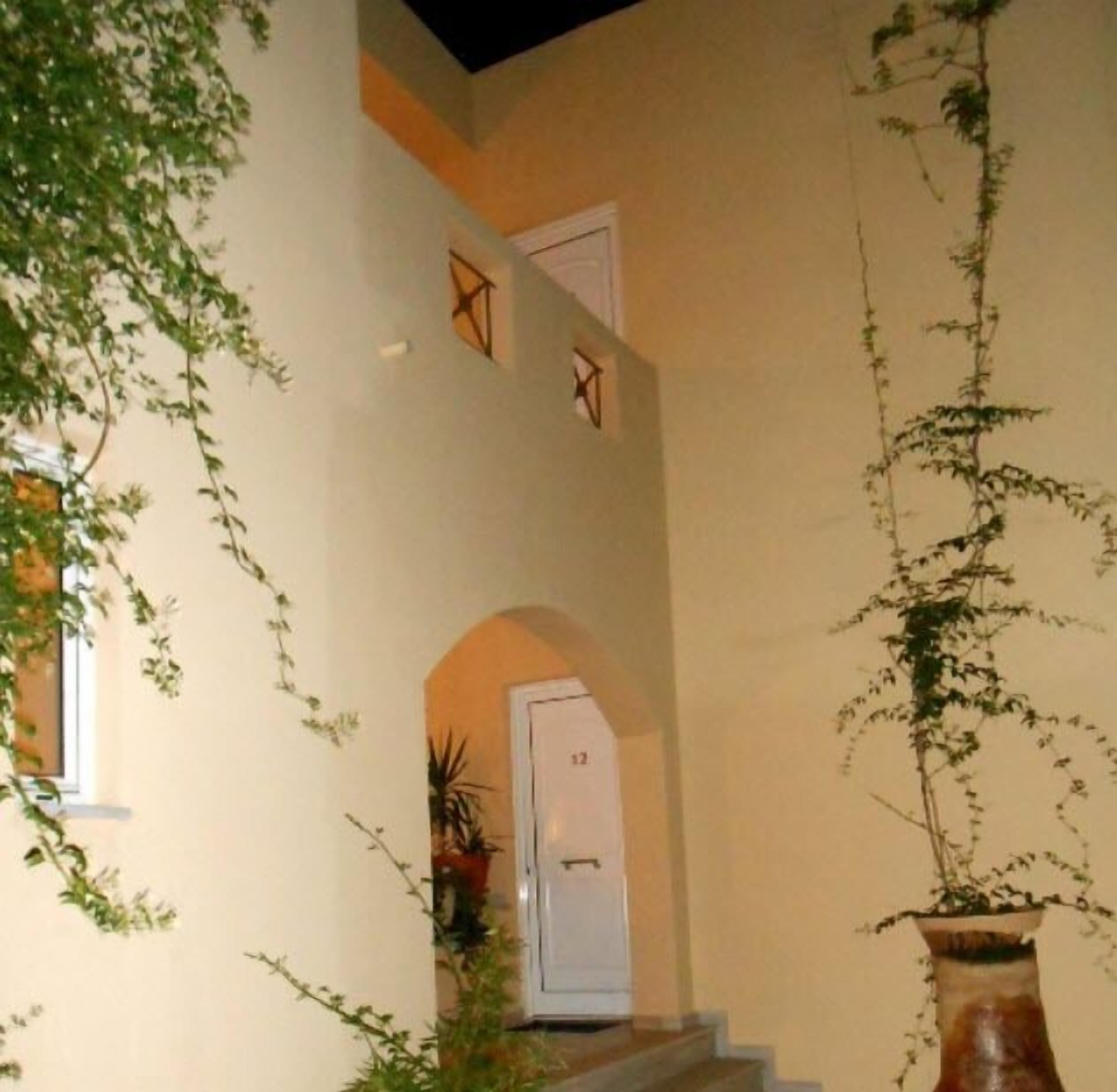 A staircase leading to a door marked with the number 12, surrounded by greenery and a large vase.