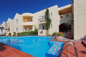 Una piscina con tobogán, rodeada de edificios de varios pisos con balcones y mobiliario exterior.