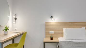 Habitación de hotel moderna con tablero de cabecera de madera, un escritorio con silla, una mesita de noche con planta y una cama con colcha gris.