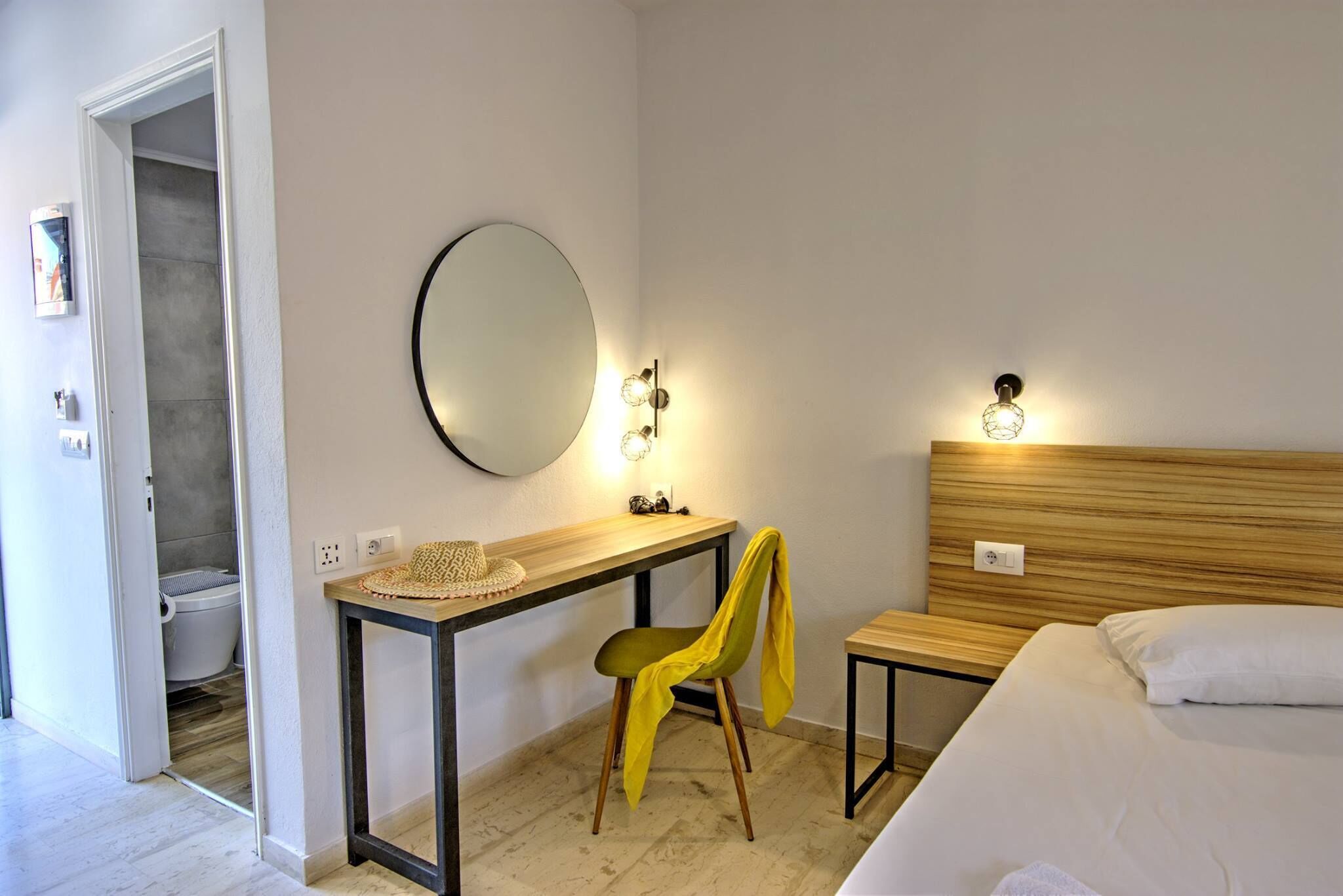 A hotel room with a bed, a desk with a mirror, a chair, and a small table.
