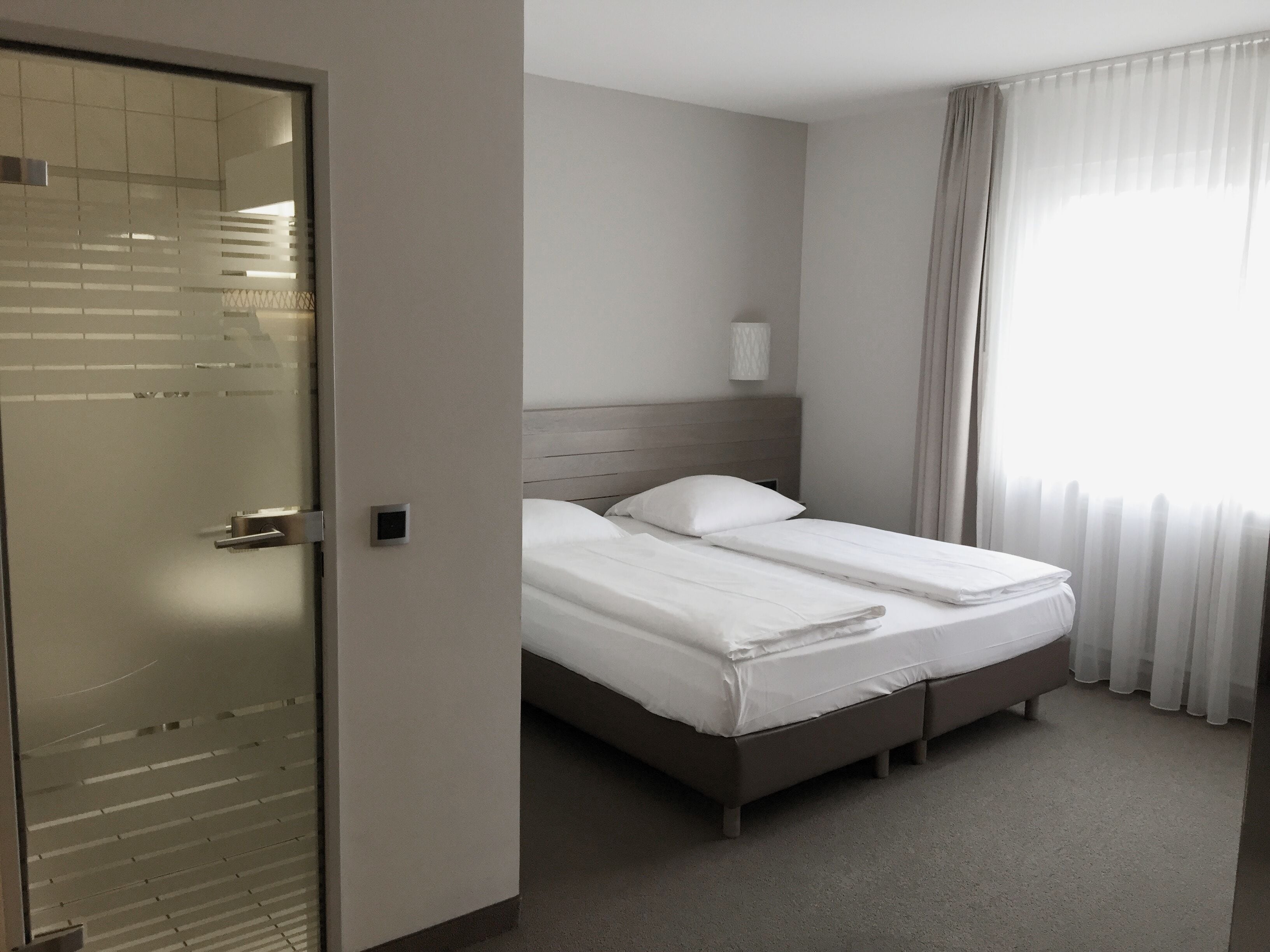 A hotel room with a bed, a wardrobe, and a window with curtains.