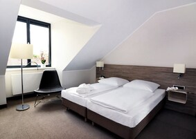 Quarto de hotel moderno com uma cama, escrivaninha, cadeira e janela.