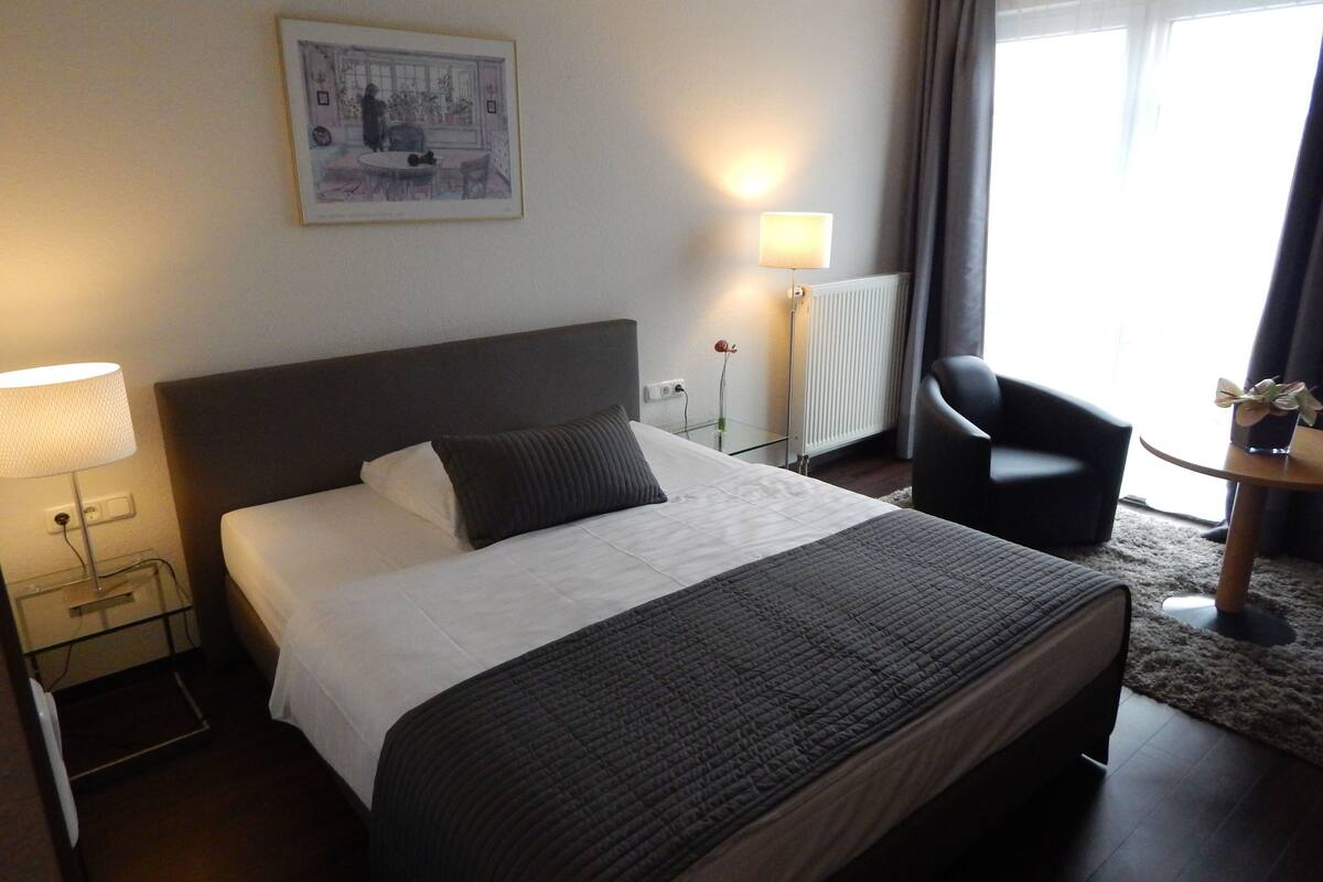 Ein Hotelzimmer mit Bett, Nachttisch, Lampe, Stuhl und einem Bild an der Wand.