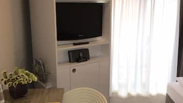 Quarto de hotel com cama, escrivaninha com cadeira, televisão e planta.