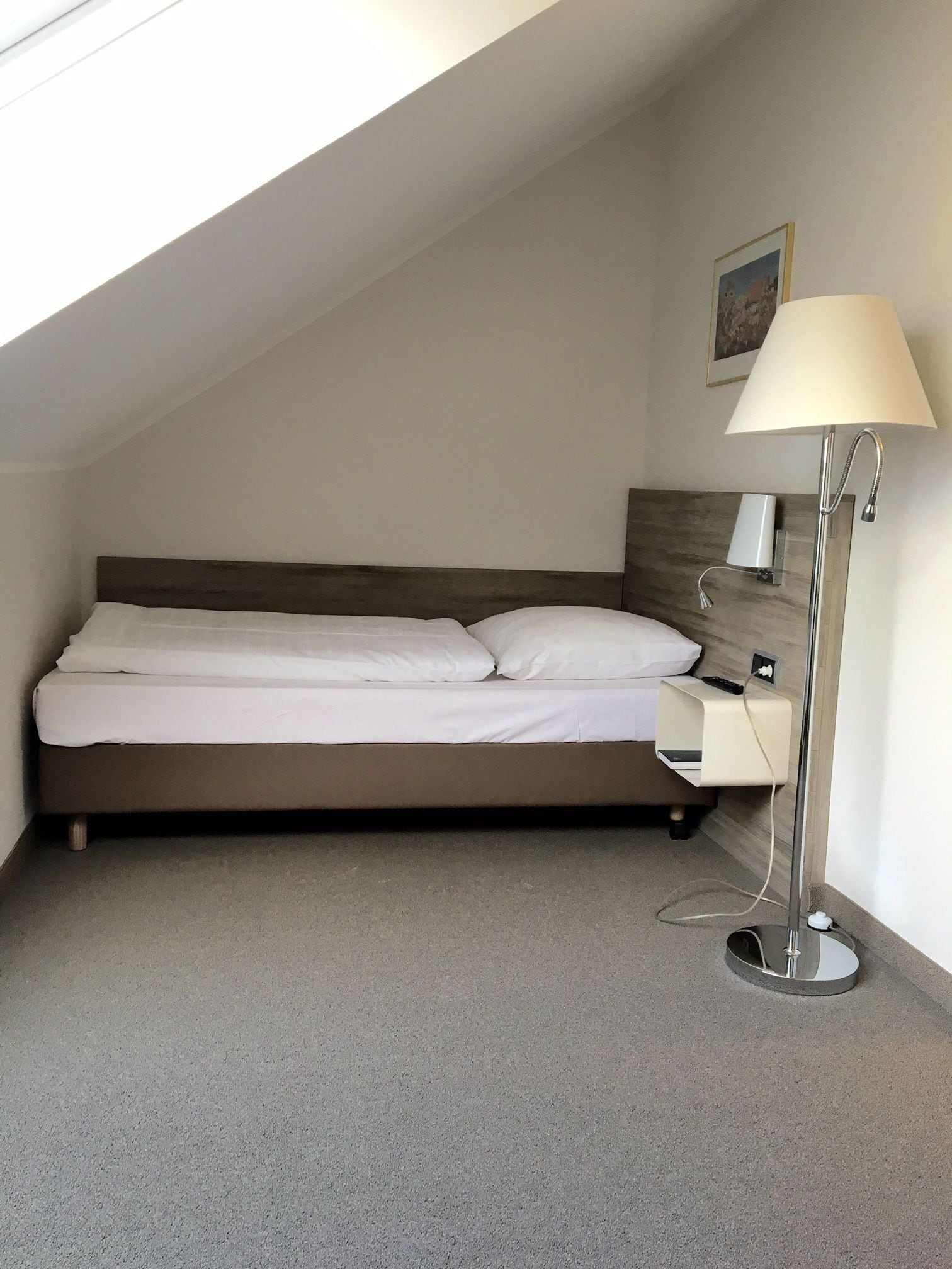 A bedroom with a bed, a bedside table, a lamp, and a painting on the wall.
