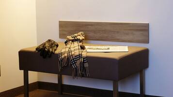 A bench with a headboard against a wall, a light fixture above, and a pair of shoes and a blanket on the bench.