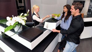 Een receptiebalie met een witte vaas vol bloemen, een zwarte toonbank en een bord met het logo van het hotel.