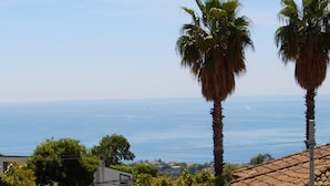 Un balcon avec une table préparée pour le thé, offrant une vue sur la côte, avec des palmiers et des maisons.