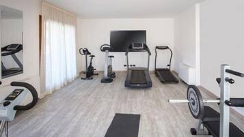 A modern hotel room with a treadmill, elliptical, stationary bike, and a TV mounted on the wall.