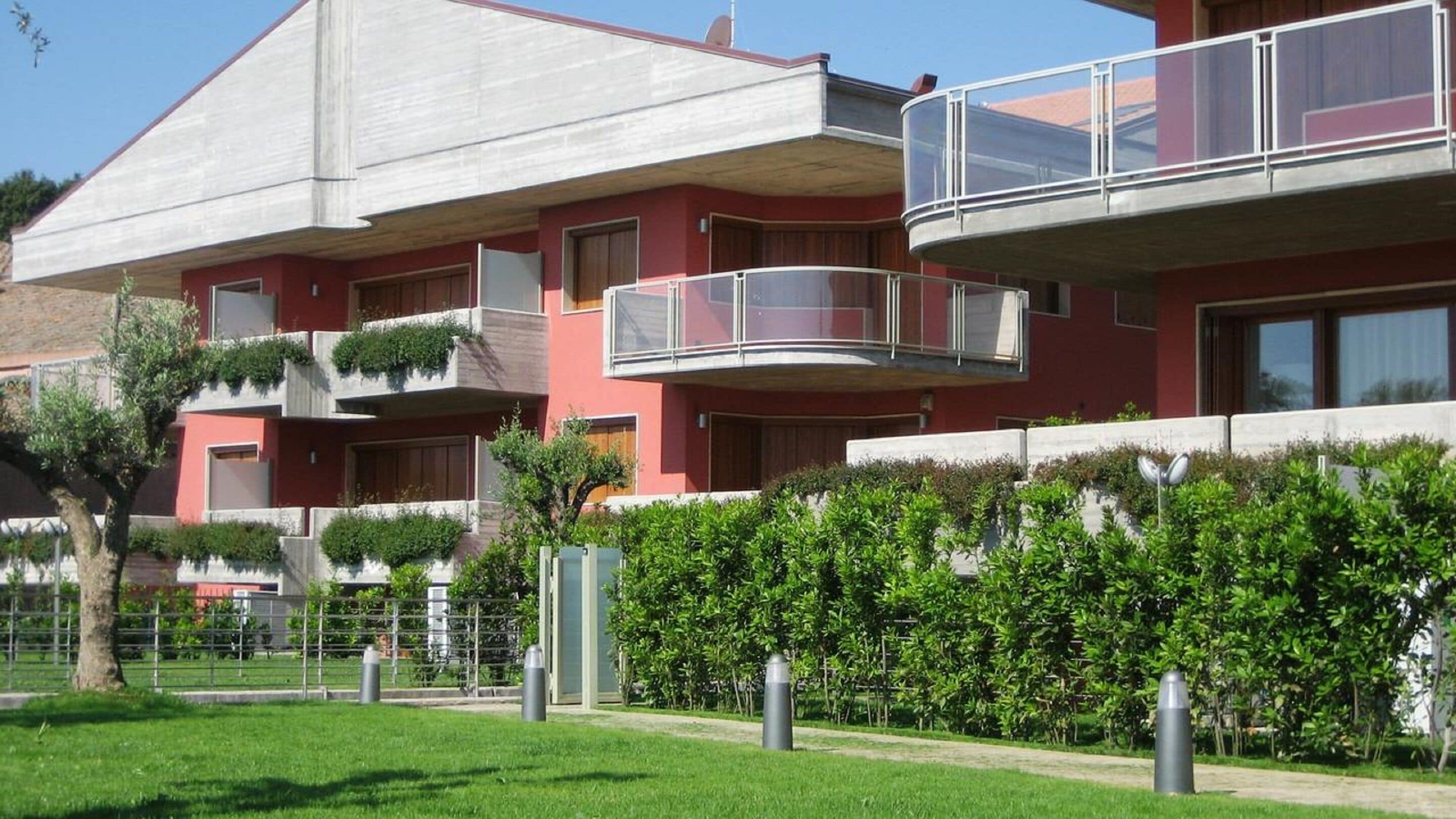 A modern apartment building with multiple balconies, a well-maintained garden, and a clear sky.