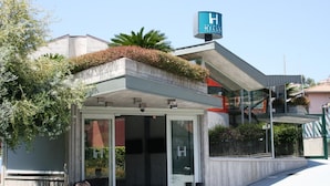 L’entrée d’un hôtel au design moderne, un espace extérieur aménagé et abrité, et une enseigne bien visible indiquant le nom de l’hôtel.
