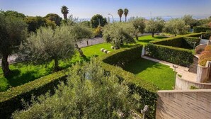 Un jardin aménagé avec des haies taillées avec soin, une variété d’arbres et une vue dégagée sur la mer.