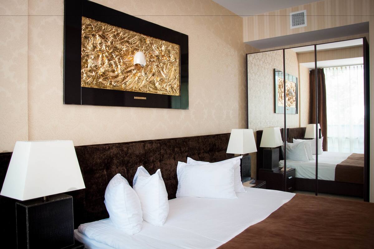 A hotel room with a large bed, two bedside tables with lamps, a wall-mounted artwork, and a sliding door leading to a balcony.