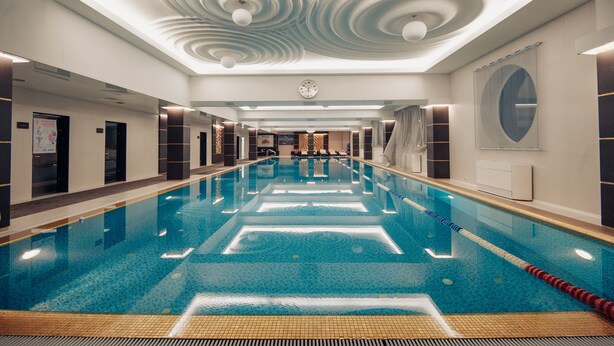 Una amplia piscina cubierta con carriles delimitados, un diseño moderno de techo y un reloj en la pared.