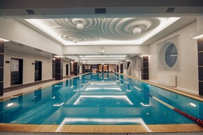 Uma grande piscina interior com pistas demarcadas, design de teto moderno e um relógio na parede.