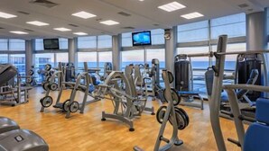 Un gimnasio con diverso equipamiento de ejercicio, amplias ventanas y vista al mar.
