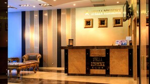 Un área de recepción con un mostrador identificado como "Stella Residence Club". Hay un sofá de cuero y un revestimiento de pared con motivos decorativos detrás del mostrador.