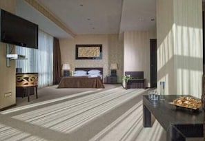 A hotel room with a large bed, a flat-screen TV, a desk with a lamp, and a view of the outdoors.